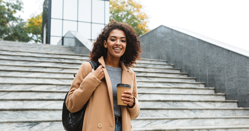 Woman smiling and holding a coffee outside on stone staircase.