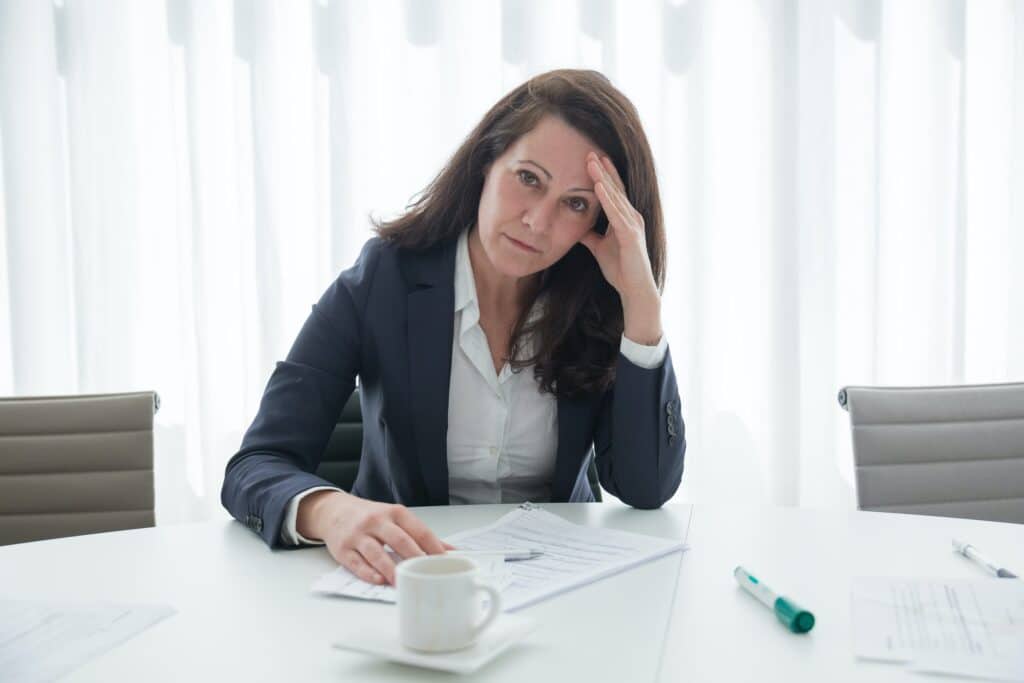 A woman sits at her desk with her hand covering her forehead.