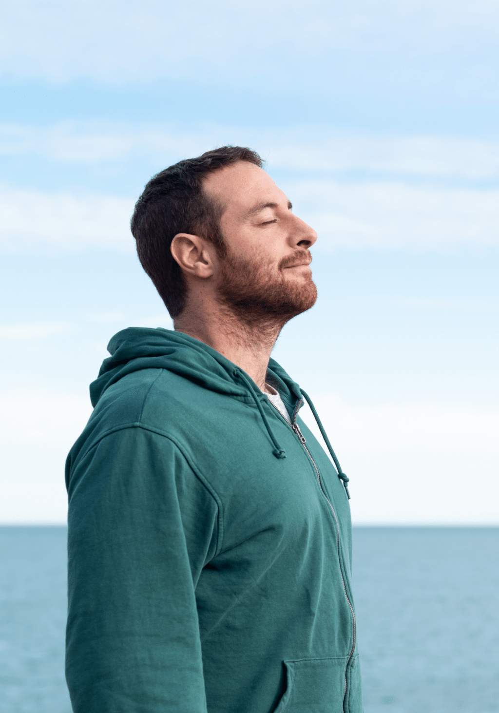 Man stands outdoors with eyes closed.